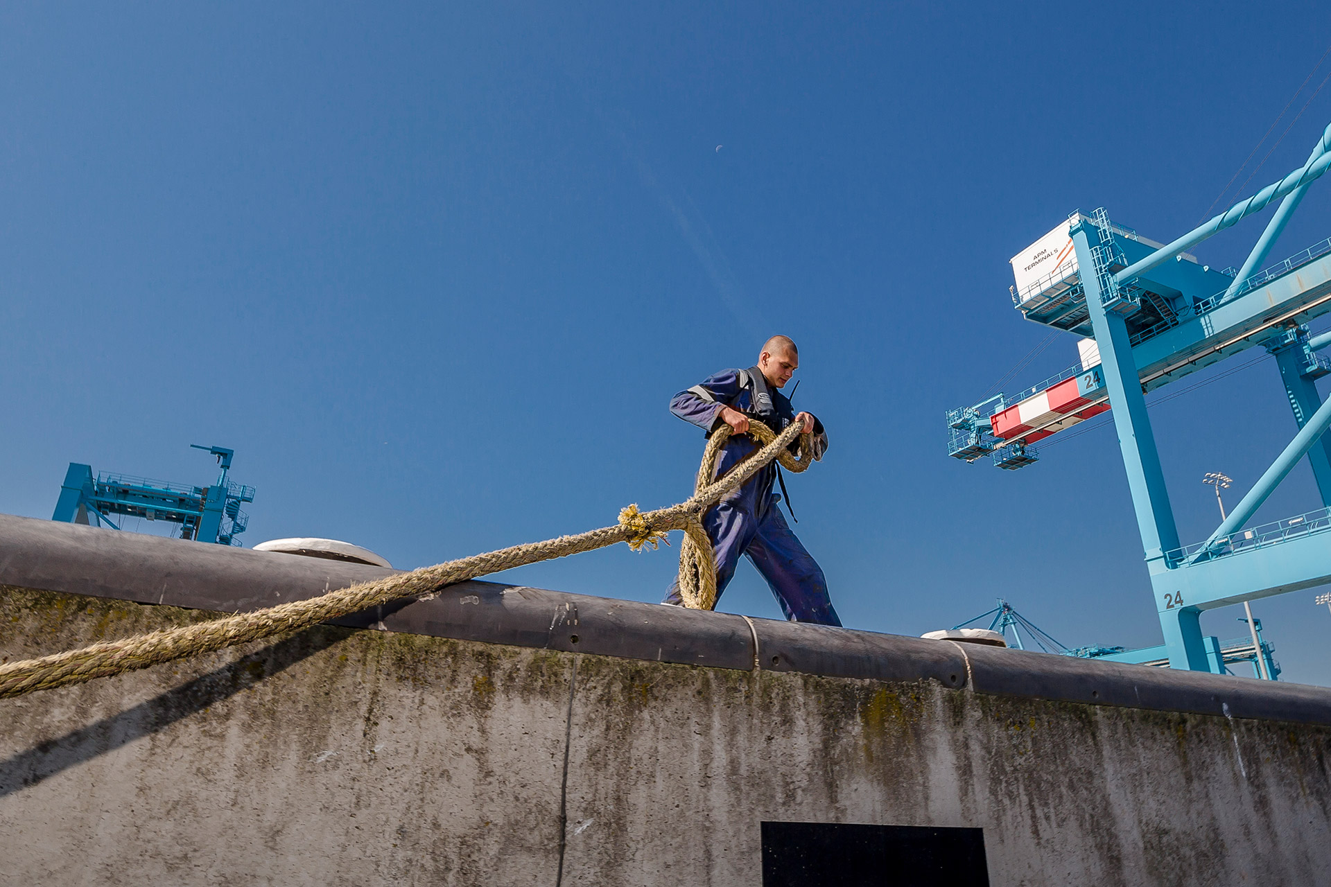 Sailor on quay moors ship with mooring line to bollard